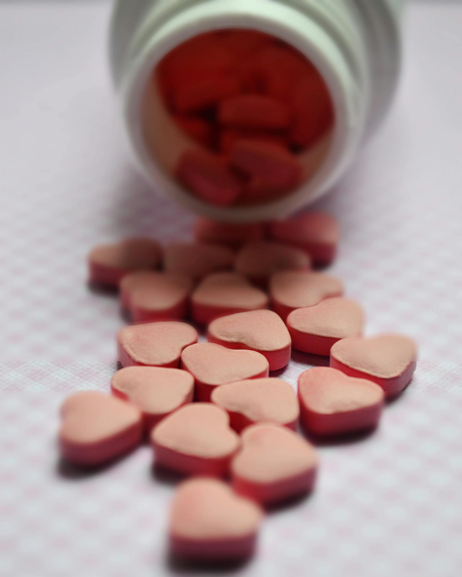 Close-up of heart-shaped pink pills spilled from a bottle on a soft surface.